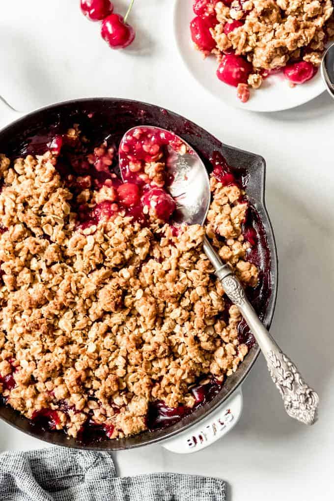 A large serving spoon scooping out a serving of cherry crisp from a cast iron skillet.