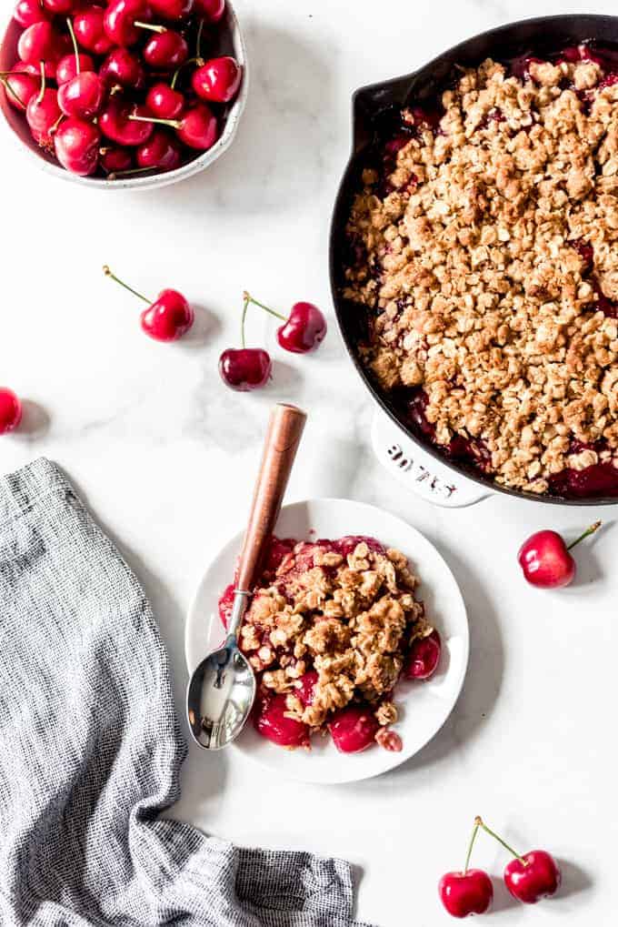 A white plate with cherry crisp next to a skillet with the rest of the cherry crisp.