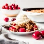A serving of cherry crisp topped with vanilla ice cream on a white plate.