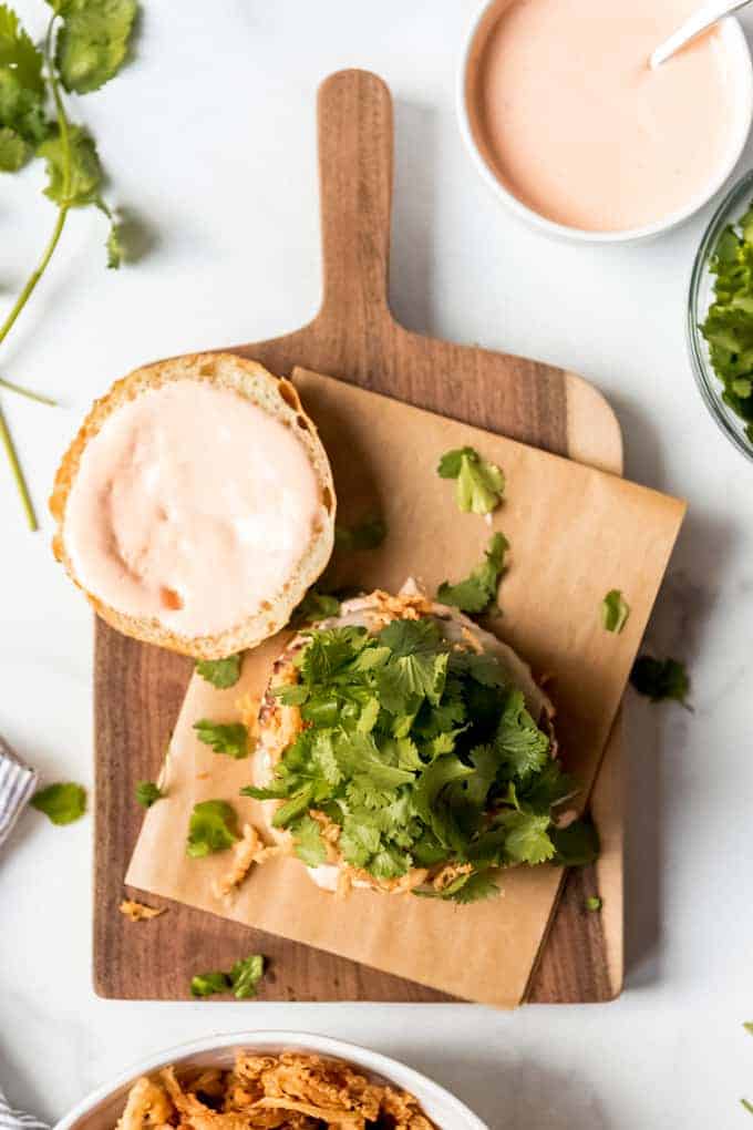 An image of hamburger buns topped with sriracha lime mayo and cilantro leaves.