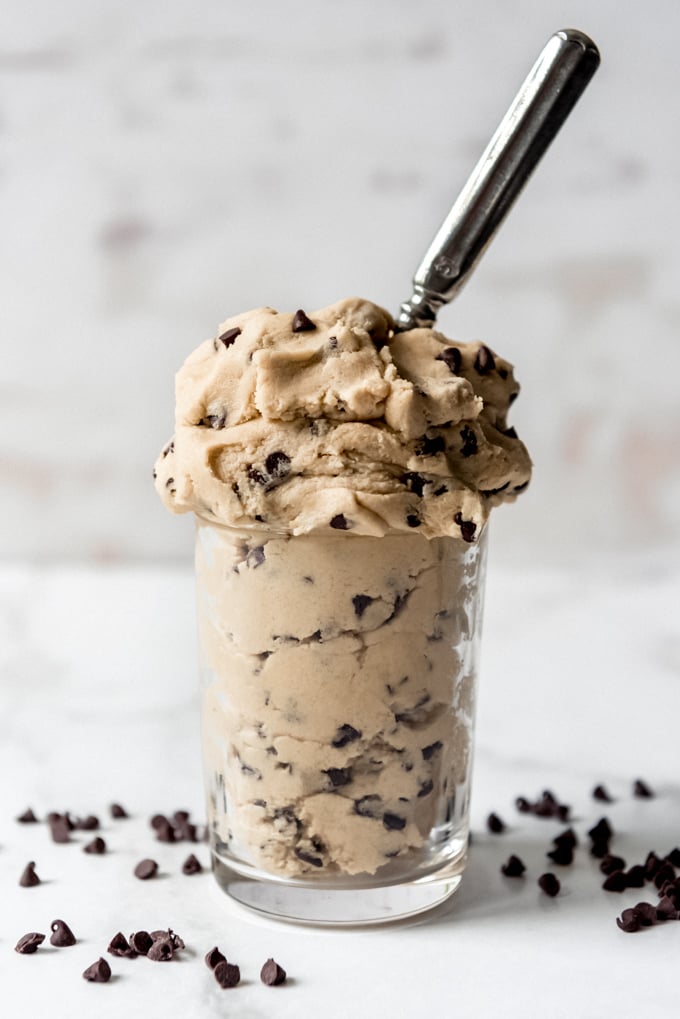 A glass full of eggless chocolate chip cookie dough with a spoon in it.
