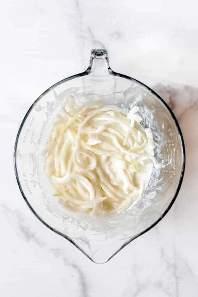 A large glass bowl with thinly sliced onions soaking in buttermilk.