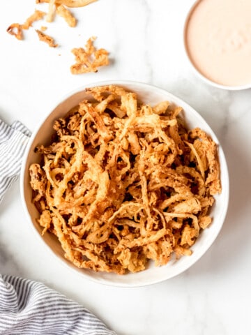 A white bowl filled with crispy fried onion strings.