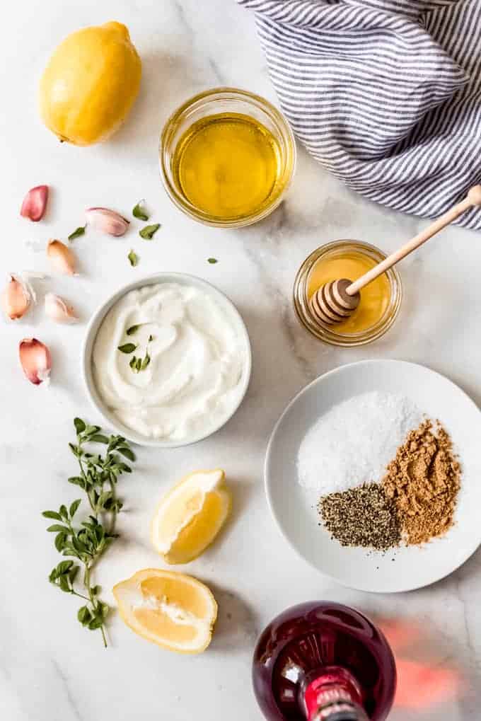 The ingredients for greek marinade arranged in individual bowls on a white marble surface.