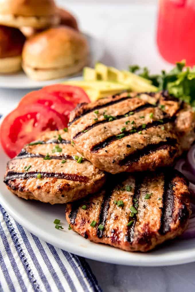 Grilled turkey burger patties on a white plate with burger toppings.