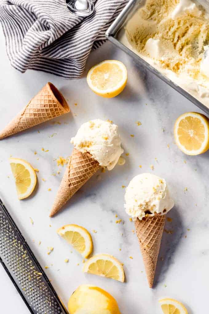 Scoops of lemon ice cream on sugar cookies on a marble surface surrounded by sliced lemons.