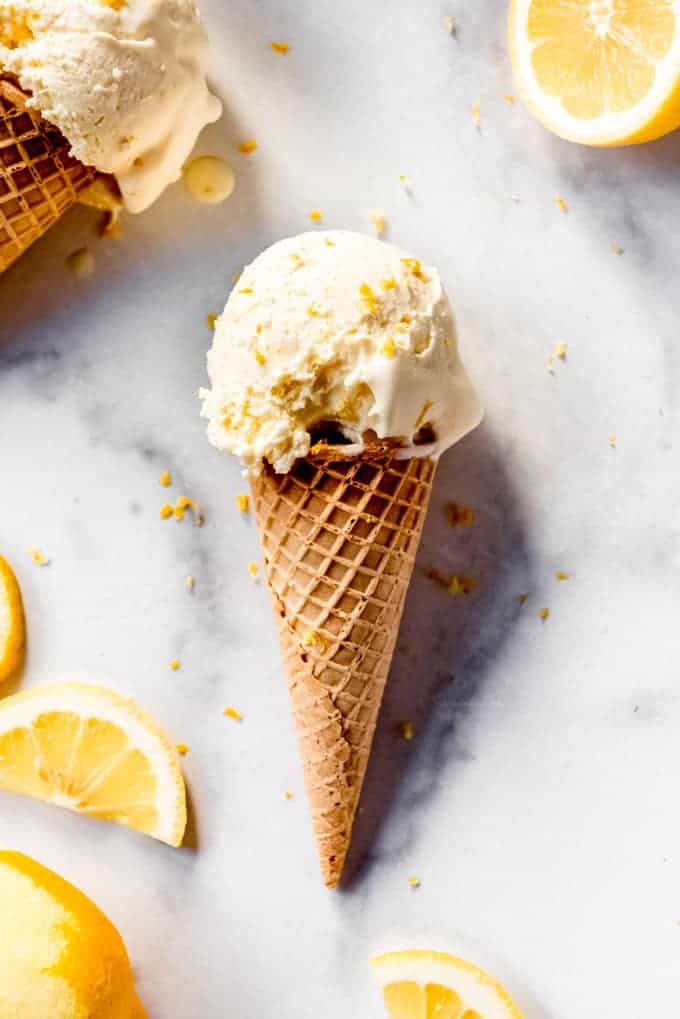 A sugar cone topped with lemon ice cream next to lemon slices.