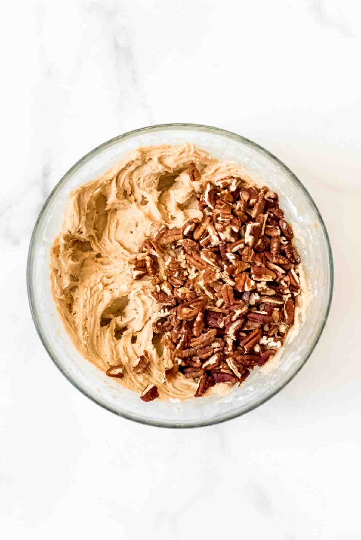 A glass mixing bowl full of blondie batter and chopped pecans.