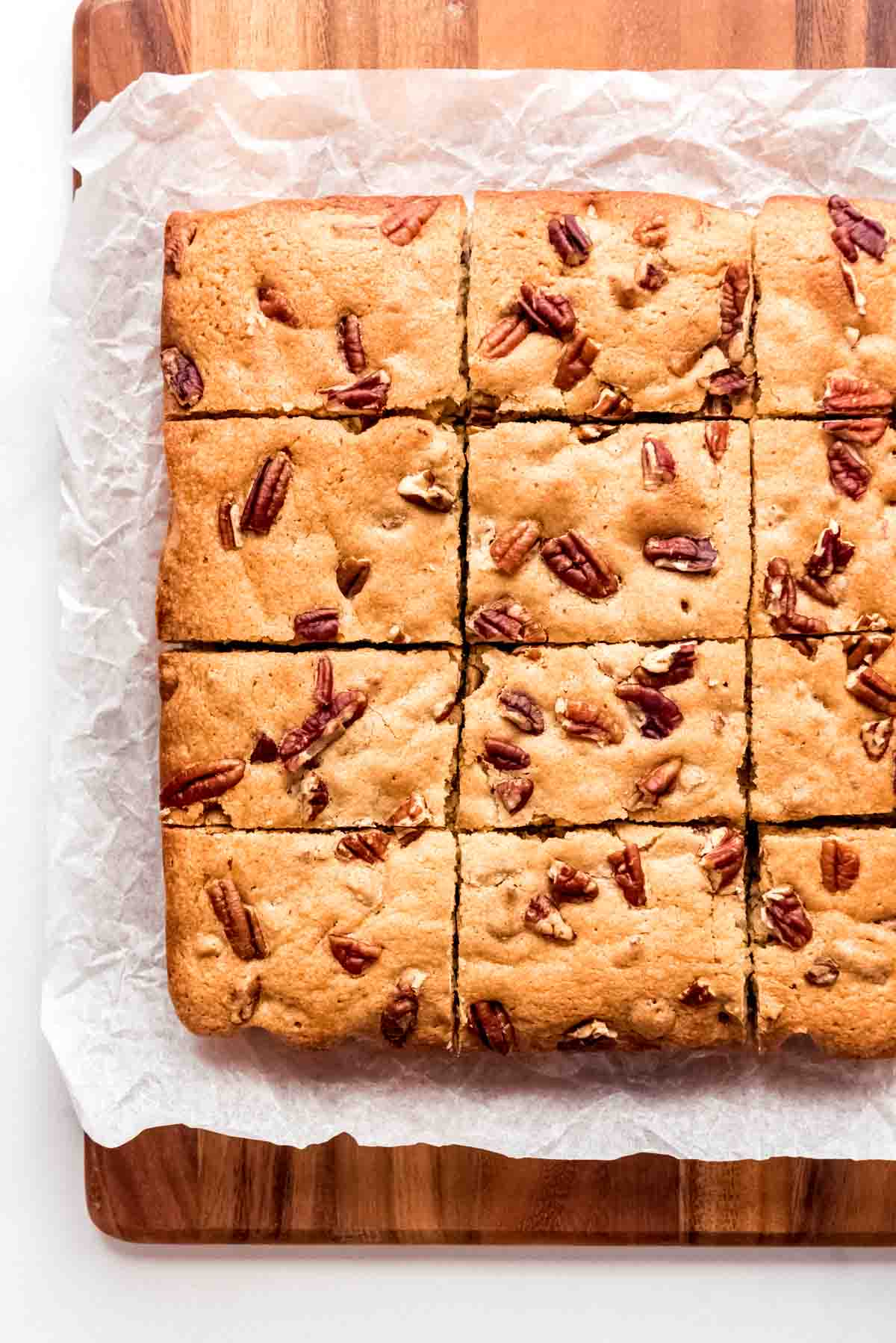 Blonde brownie squares topped with pecans on white parchment paper.