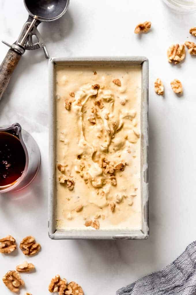 A bread pan filled with maple walnut ice cream next to a glass pitcher of syrup and walnuts.