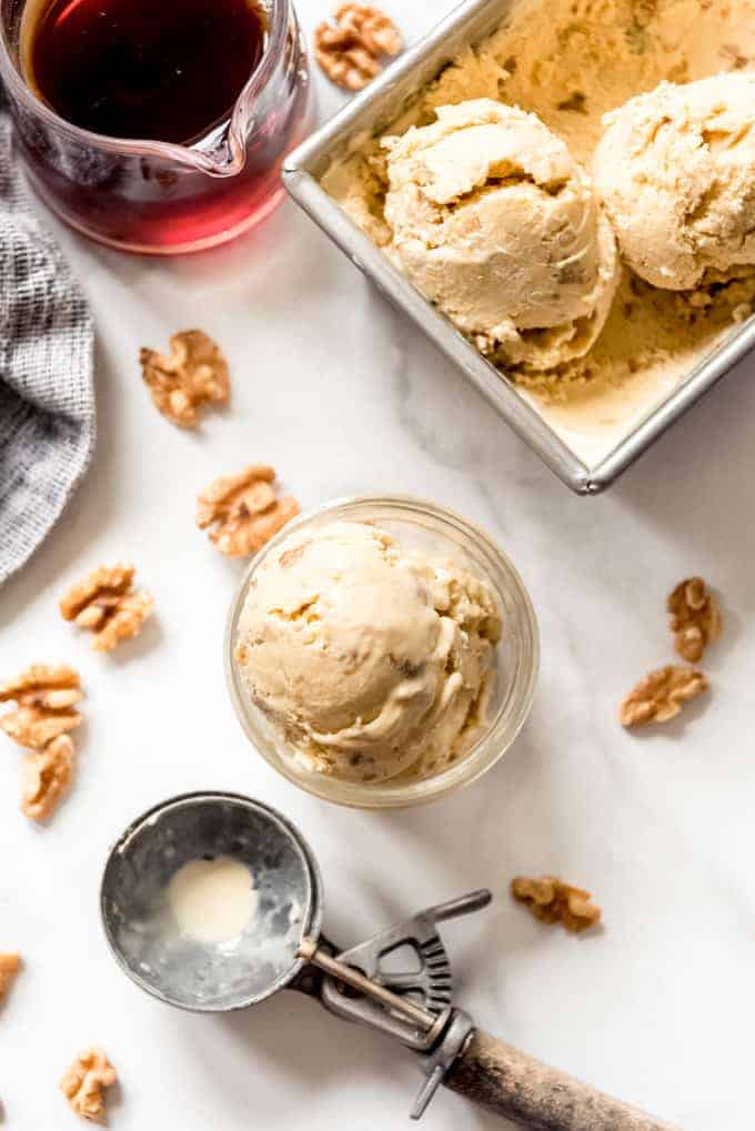 A scoop of maple walnut ice cream next to more scoops of the homemade ice cream in a bread pan.