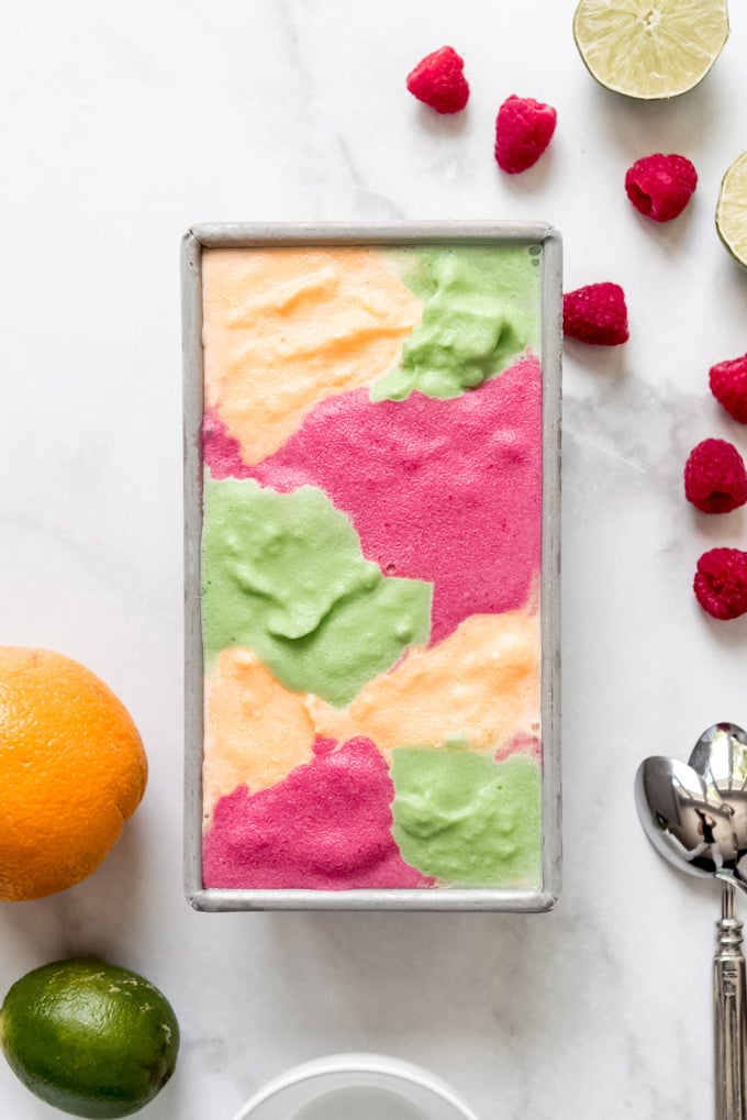 A metal bread pan filled with lime, orange, and raspberry sherbet.