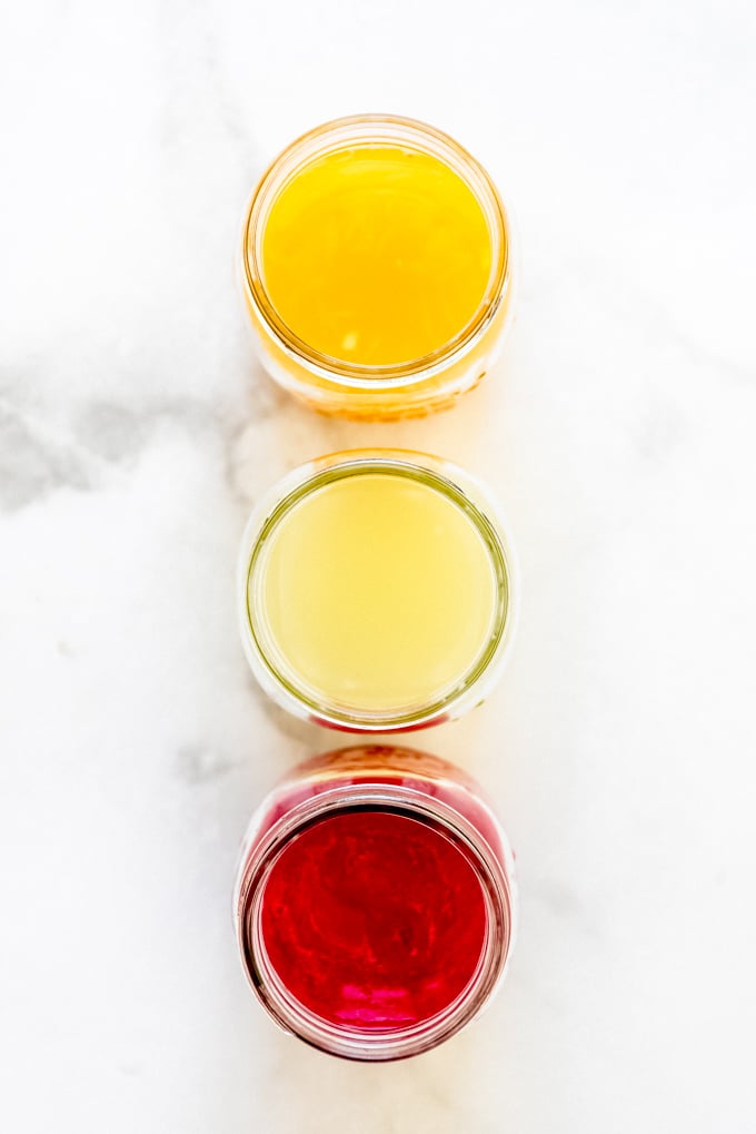 Three glass jars filled with orange juice, lime juice, and raspberry puree.