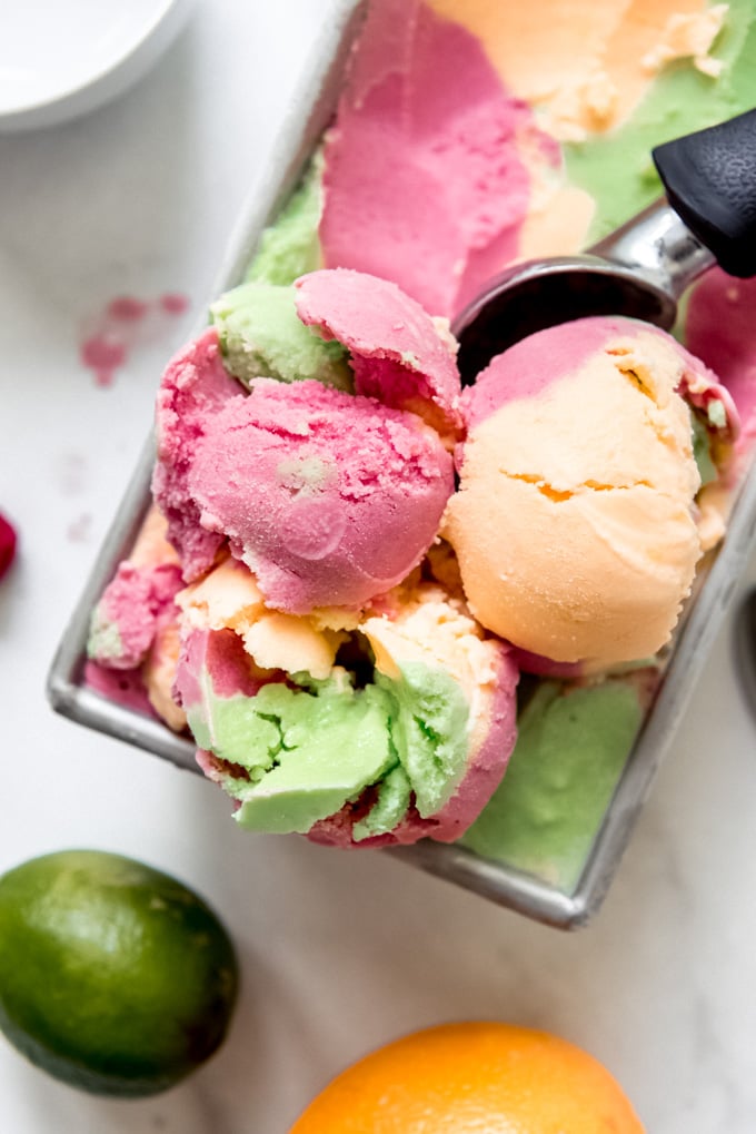 Scoops of orange, raspberry, and lime sherbet in a bread pan.