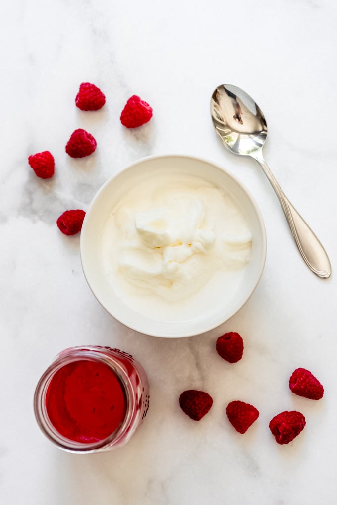 A white bowl filled with sherbet base next to raspberry puree.