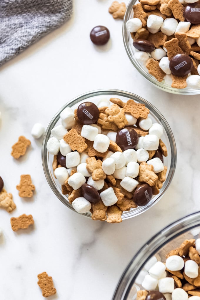 A glass bowl full of mini marshmallows, Teddy Grahams, and Hershey's chocolate candy.