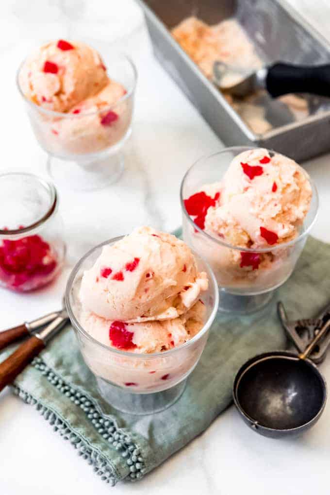 Bowls of homemade tutti-frutti ice cream next to a jar of maraschino cherries and an ice cream scoop.