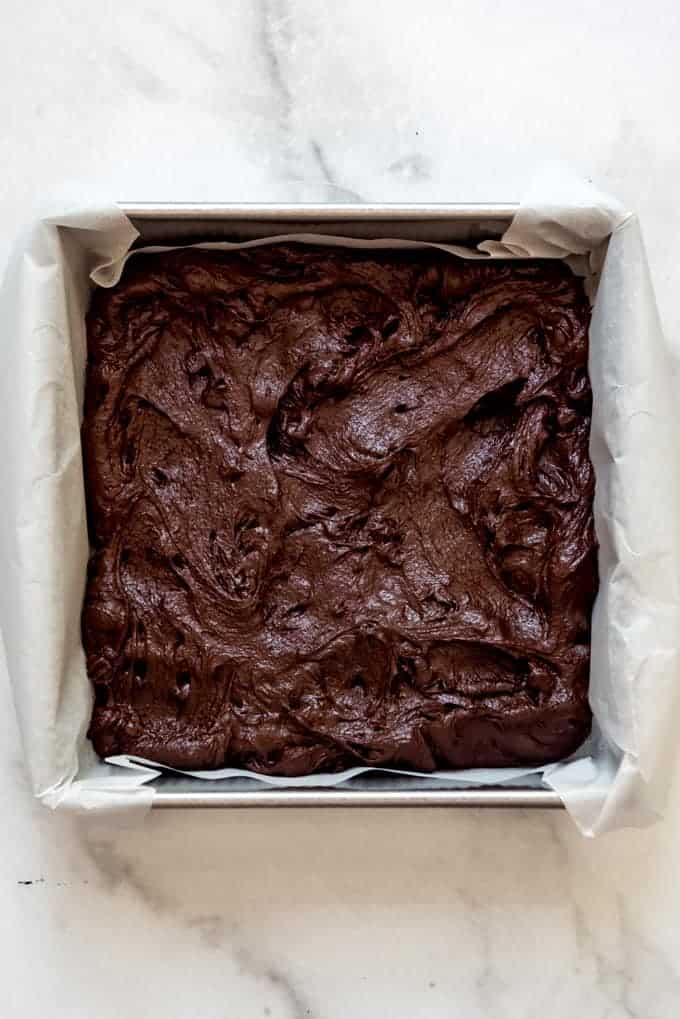 Brownie batter in a pan lined with parchment paper.