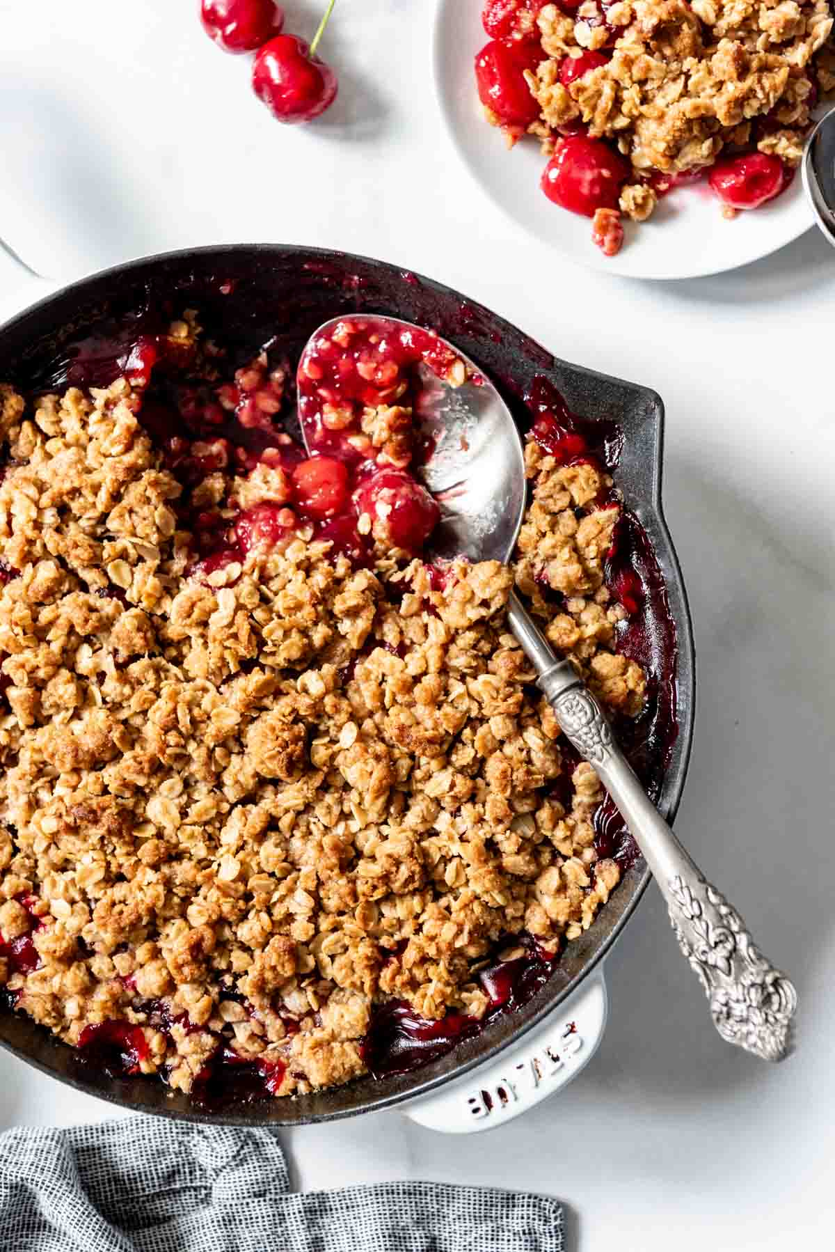 A large serving spoon scooping out a serving of cherry crisp from a cast iron skillet.