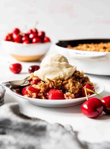 A serving of cherry crisp topped with vanilla ice cream on a white plate.