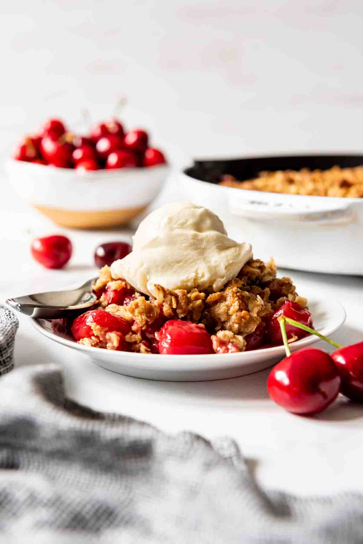 A serving of cherry crisp topped with vanilla ice cream on a white plate.