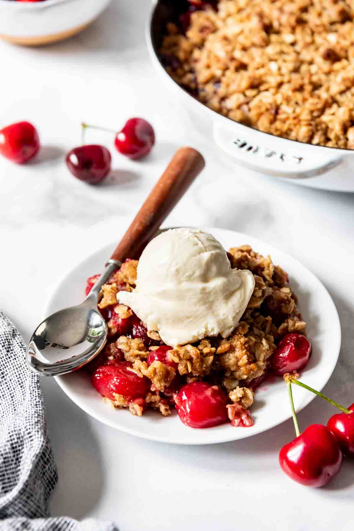 Cherry crisp on a white plate with a scoop of vanilla ice cream.