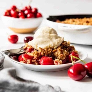 A serving of cherry crisp topped with vanilla ice cream on a white plate.