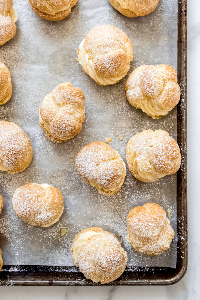 filled cream puffs on a baking sheet and dusted with powdered sugar
