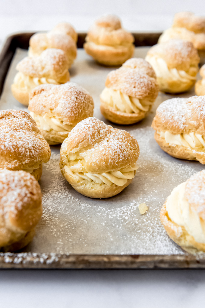 Homemade cream puffs dusted with powdered sugar on a baking sheet.