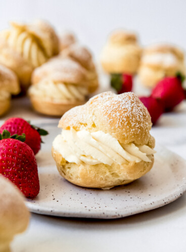 A cream puff filled with pastry cream on a plate with strawberries.