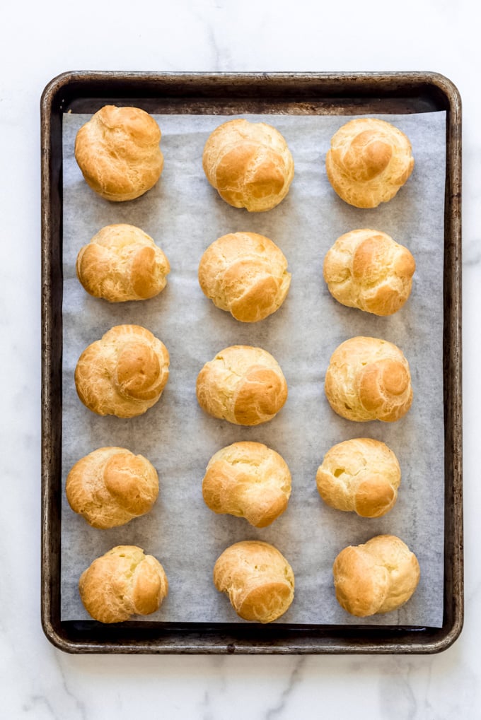 Baked cream puffs on a parchment lined baking sheet