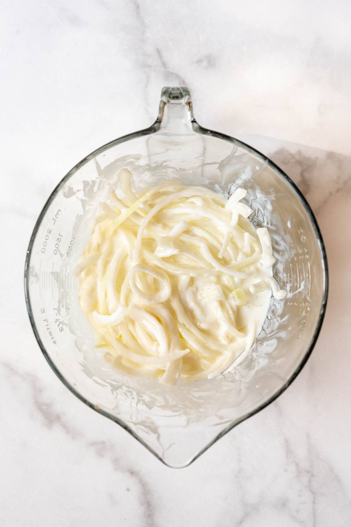 A large glass bowl with thinly sliced onions soaking in buttermilk.