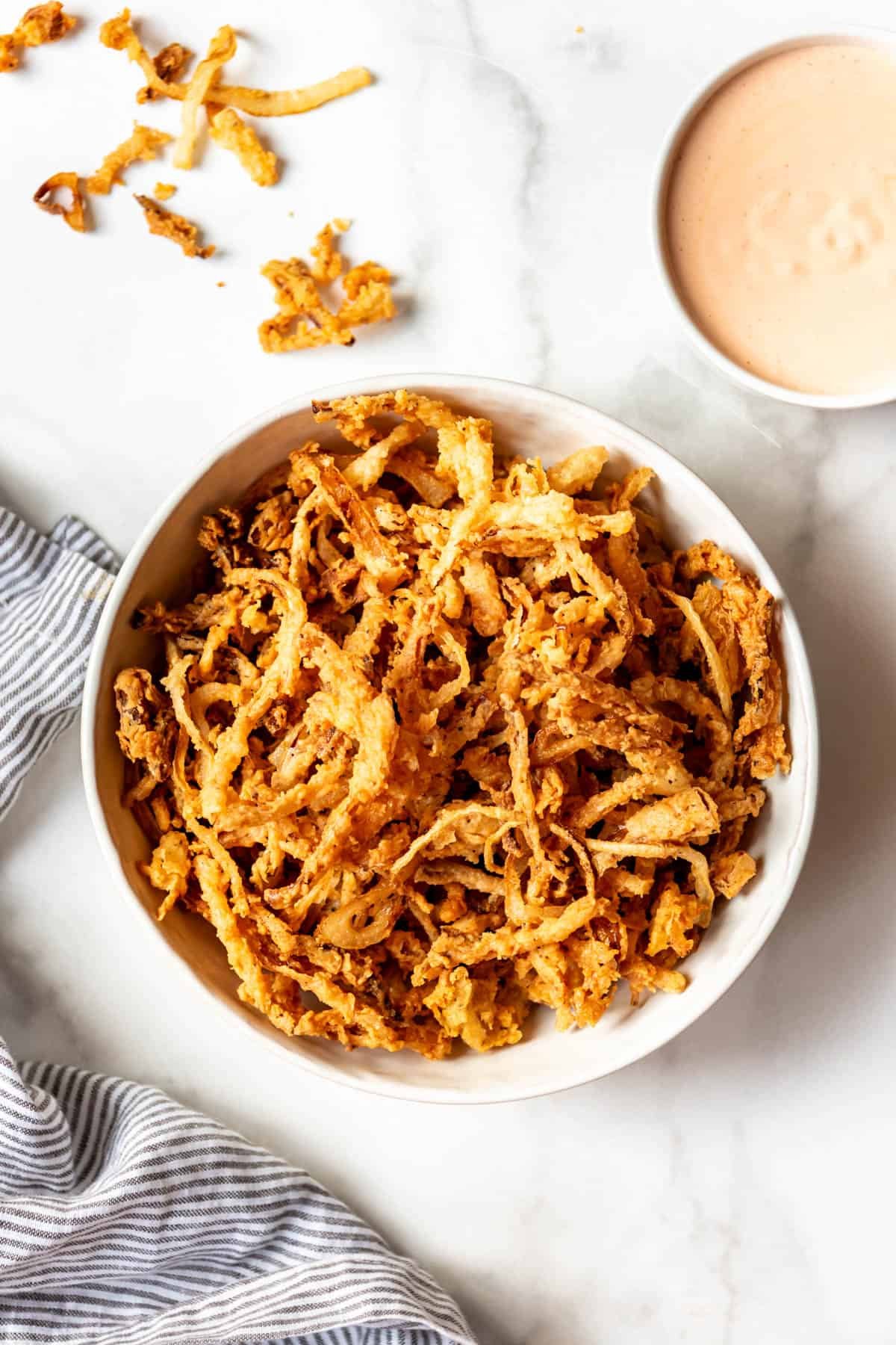 A white bowl filled with crispy fried onion strings.