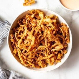 A white bowl filled with crispy fried onion strings.