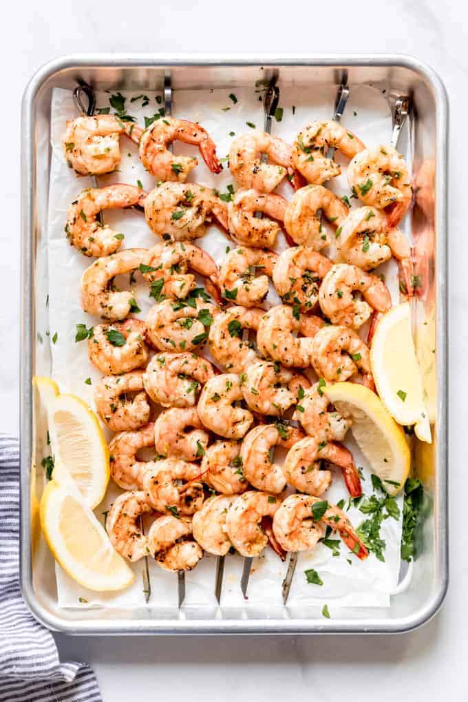 grilled shrimp skewers on parchment paper and baking tray, with lemon wedges