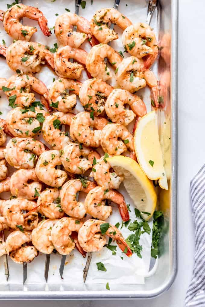 grilled shrimp skewers on parchment paper and baking tray, with lemon wedges