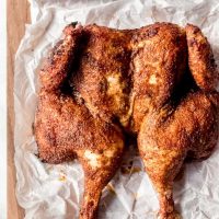 An overheat image of a butterflied smoked whole chicken on parchment paper on a cutting board.