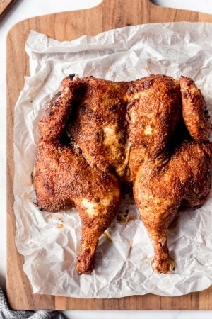 An overheat image of a butterflied smoked whole chicken on parchment paper on a cutting board.