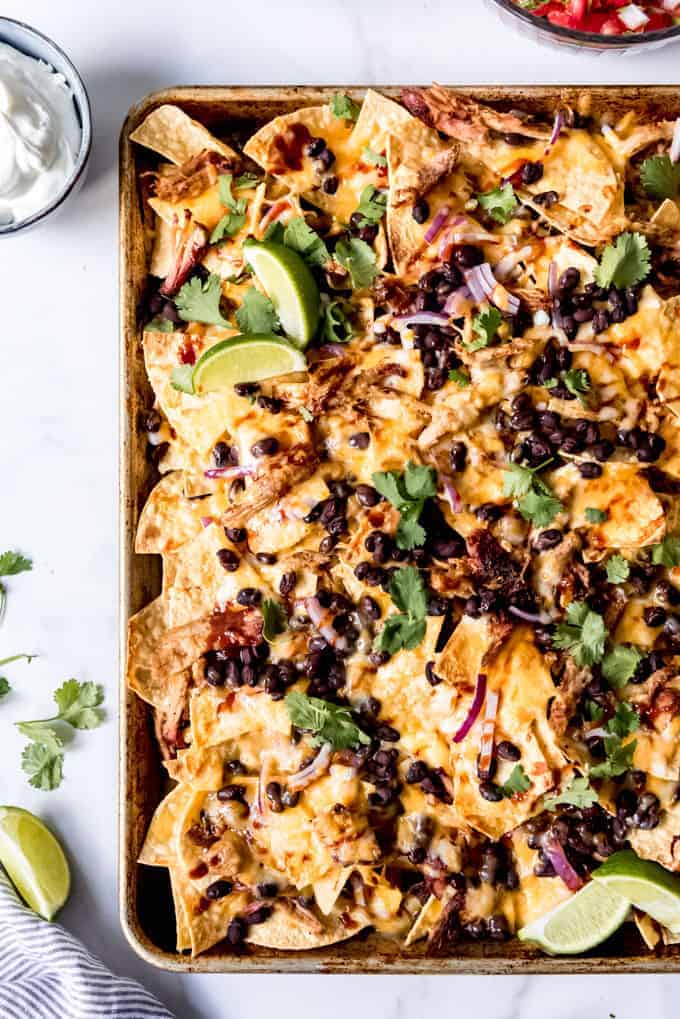 Tortilla chips with cheese, black beans, cilantro, and red onions on a baking sheet.