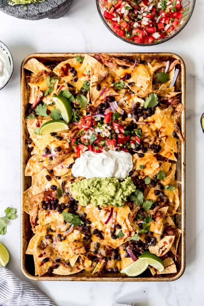 bbq pork nachos on a baking sheet topped with sour cream, guac and other toppings