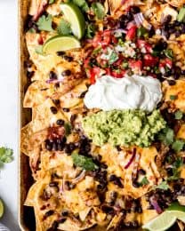 Pulled pork nachos on a baking sheet topped with guacamole, sour cream, and pico de gallo.