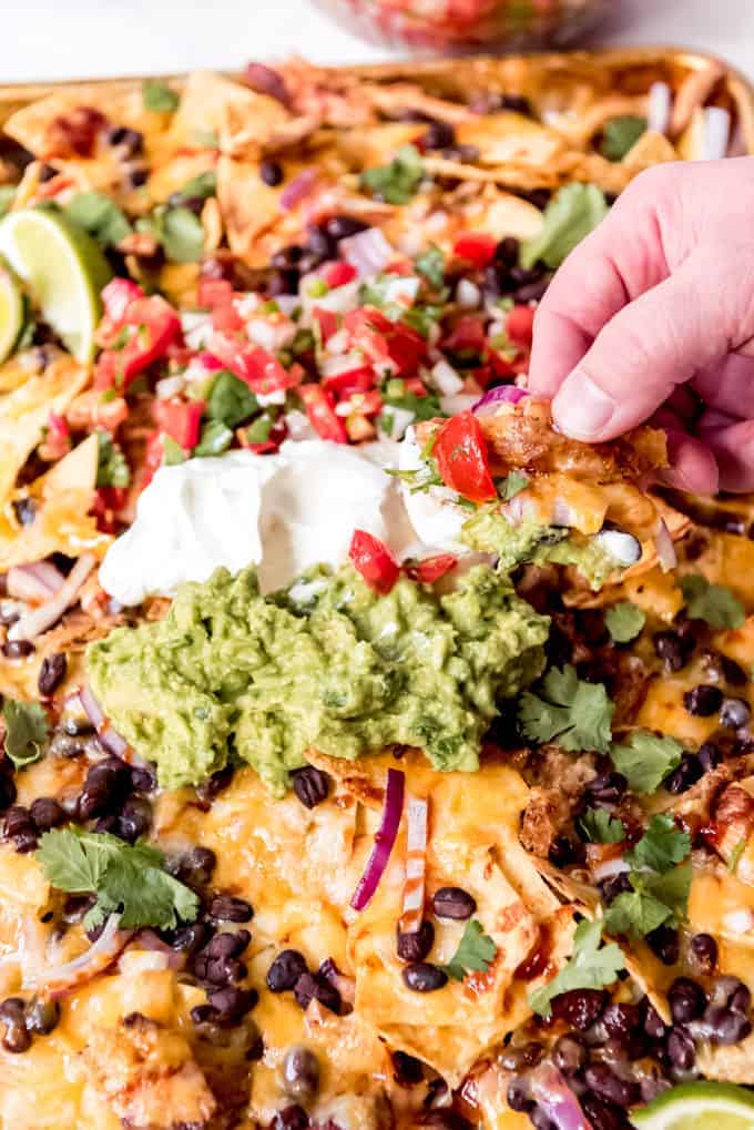 A hand scooping up a nacho chip with guacamole and sour cream on it.