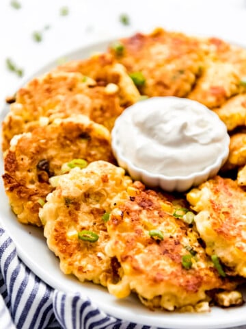 Piles of corn fritters beside a small bowl of sour cream.