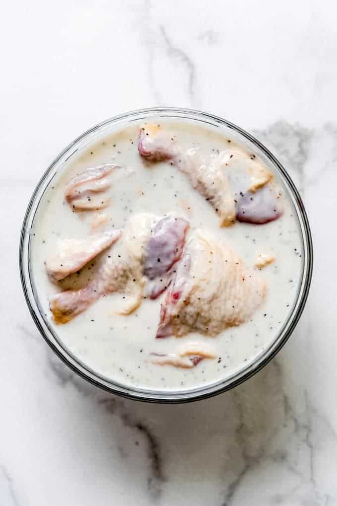 A glass bowl filled with chicken pieces in seasoned buttermilk.