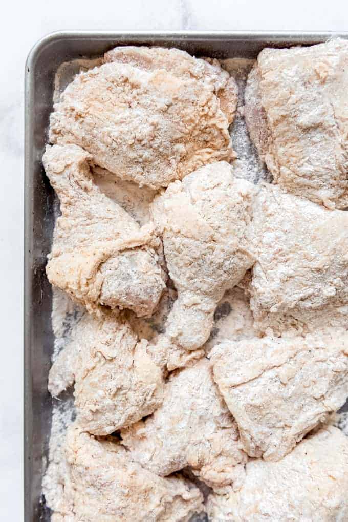 Chicken pieces coated in buttermilk and seasoned flour on a baking sheet.