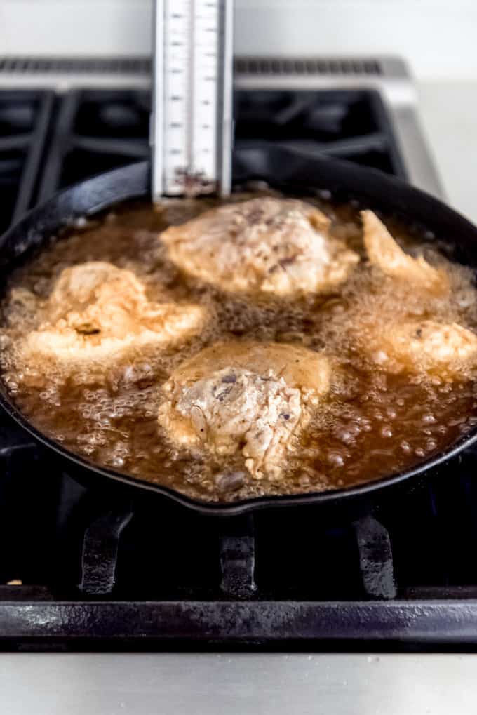 Chicken frying in hot oil in a cast iron skillet.