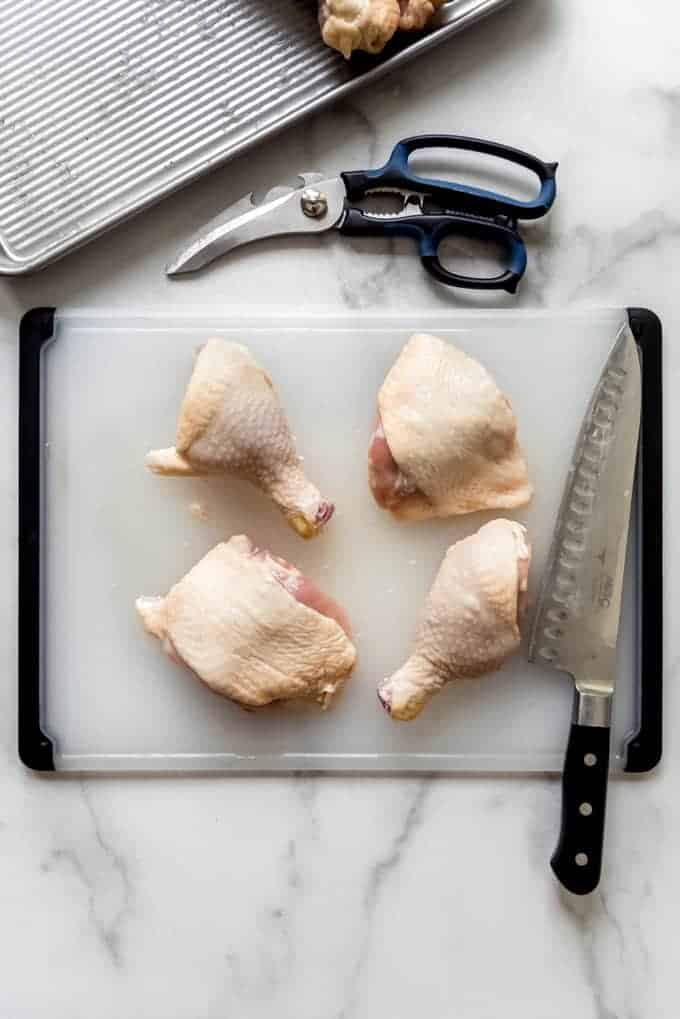 Chicken thighs and legs on a cutting board next to shears and a large knife