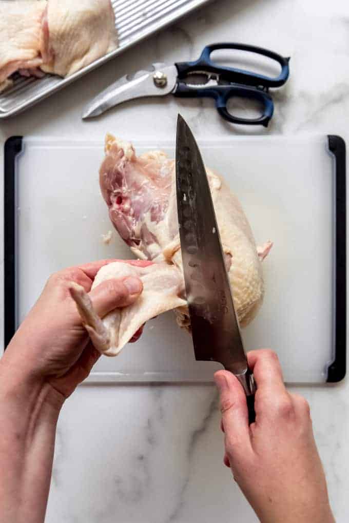 a pair of hands removing a chicken wing fromt he breast with a large knife