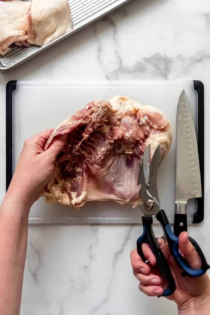 Using kitchen shears to cut the rib cage off of the chicken breast