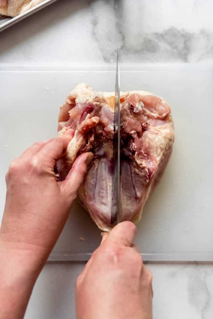 a large knife cutting between two chicken breasts to break them apart